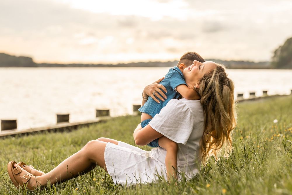 Couple embracing on a grassy hillside during sunset with water in the background.