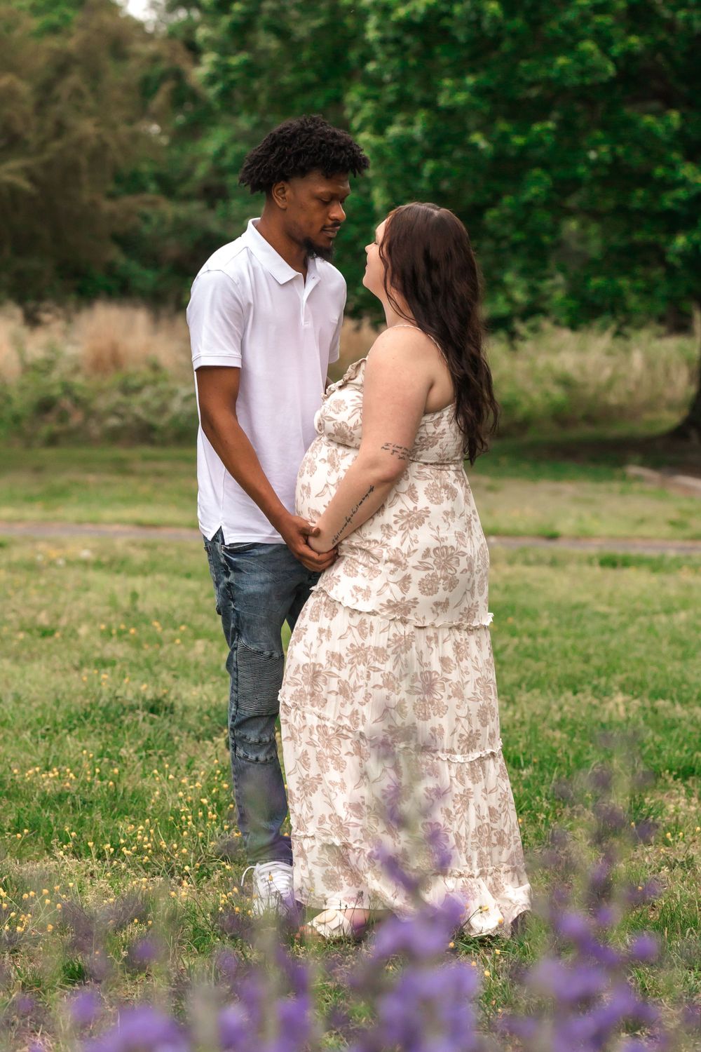 Couple standing in a meadow with purple wildflowers blooming in the foreground.