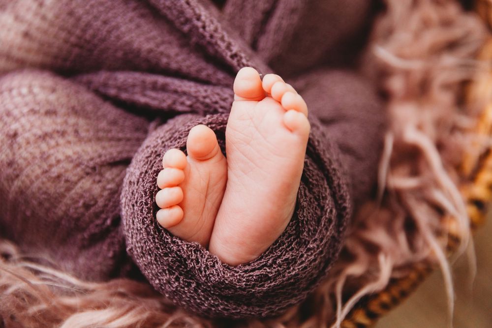 Close-up of tiny baby feet wrapped in soft purple knit blanket.