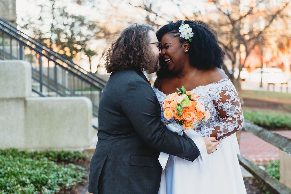 Joyful wedding couple sharing intimate moment outdoors with orange bouquet.