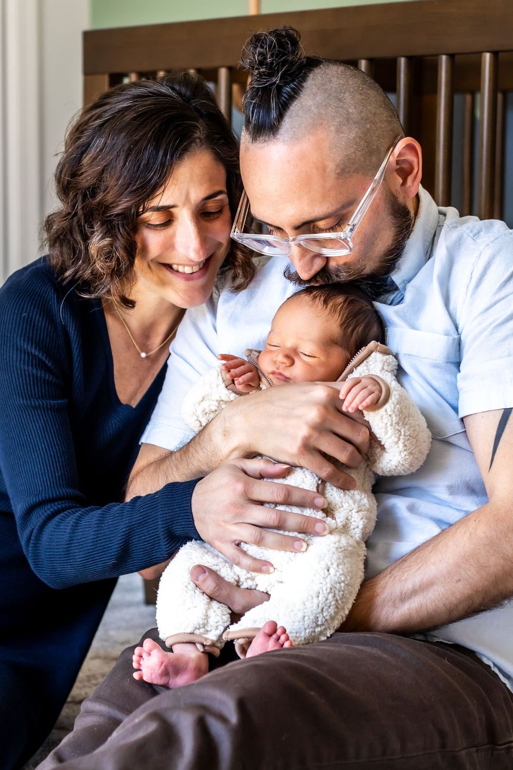 Parents lovingly gazing at their newborn baby while sitting together on wooden chair.