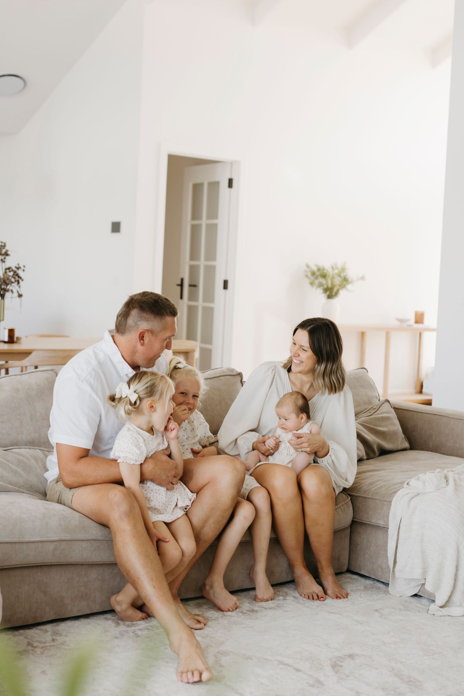 A happy family of five relaxes together on a beige sofa in a bright, modern living room.