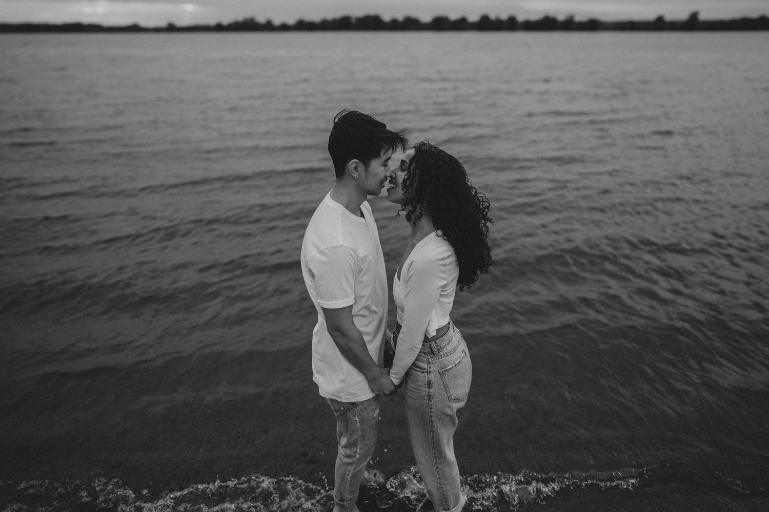 A loving couple embraces on the shoreline during sunset in black and white.