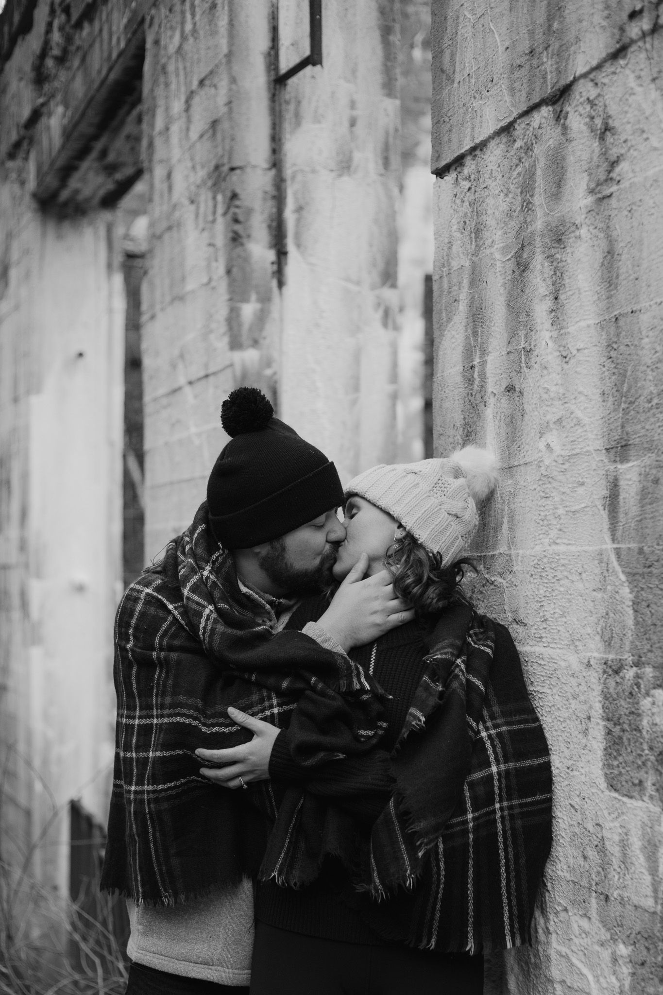 A winter romance scene with a couple sharing an intimate moment against a stone wall.