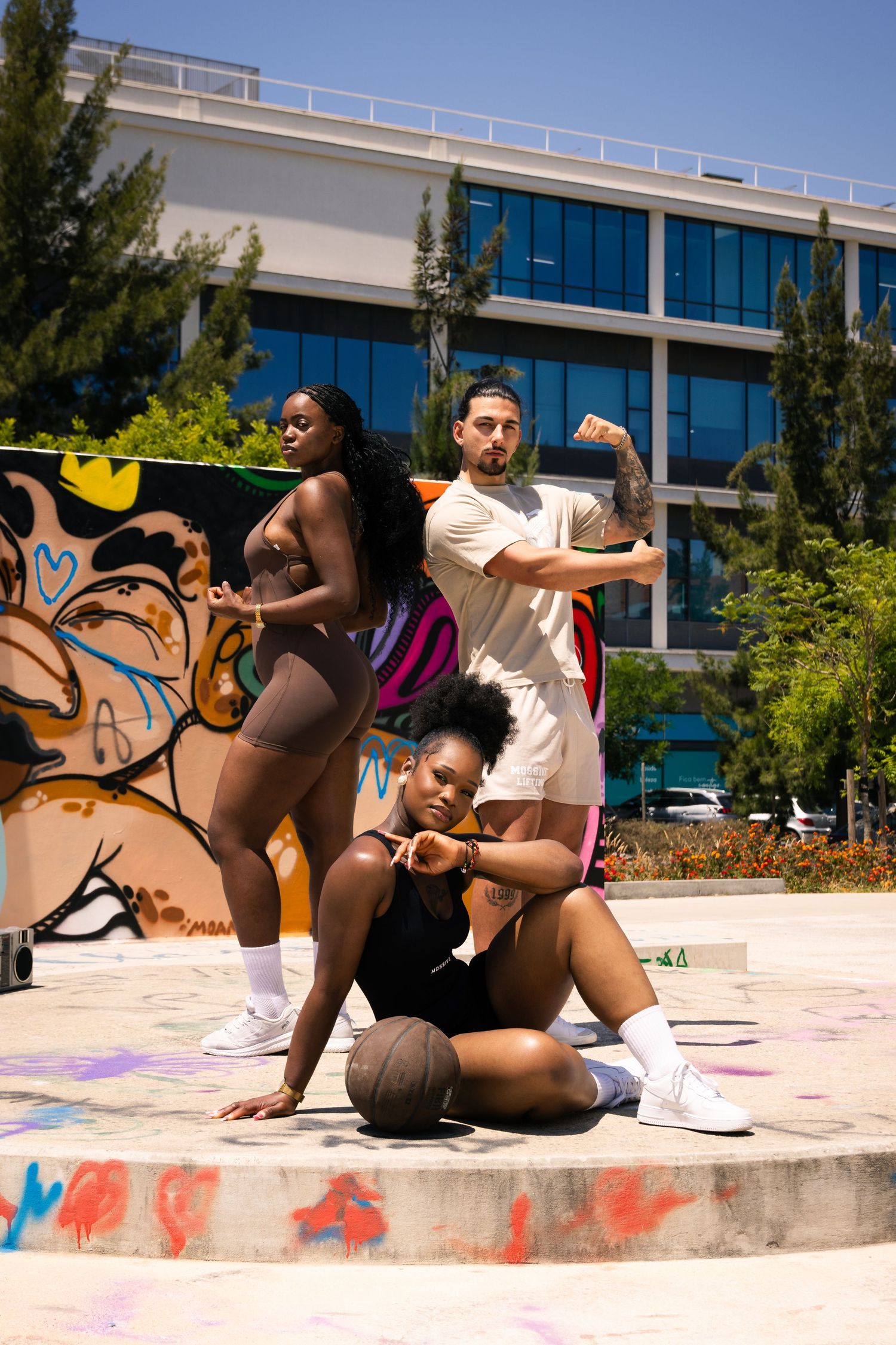 Group performs urban dance moves on concrete ledge with graffiti wall and modern building backdrop.