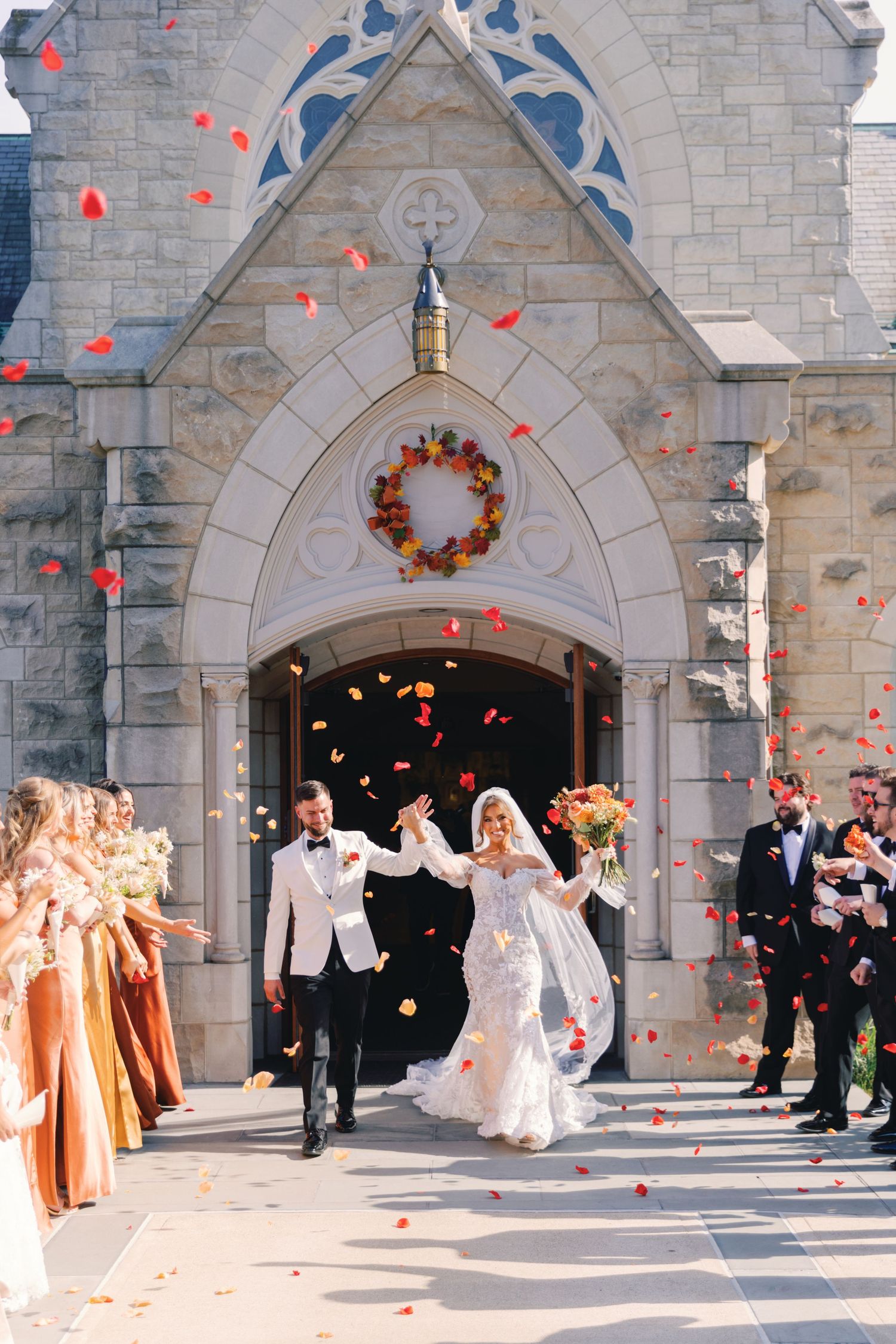 Bride and groom exit stone church as guests toss colorful fall flower petals in celebration.