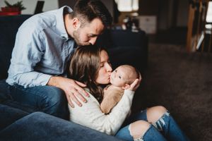 A tender family moment as parents cuddle with their newborn baby on a cozy couch.