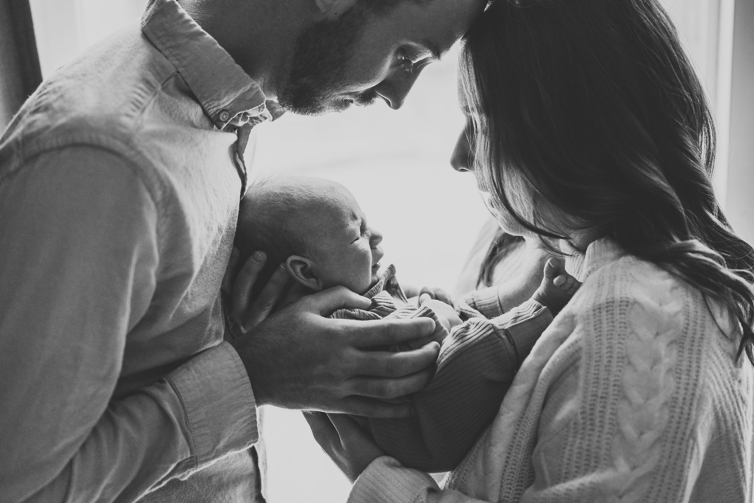 Black and white image of couple cradling newborn together.
