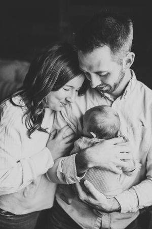 An intimate black and white portrait of parents sharing a moment with their newborn.