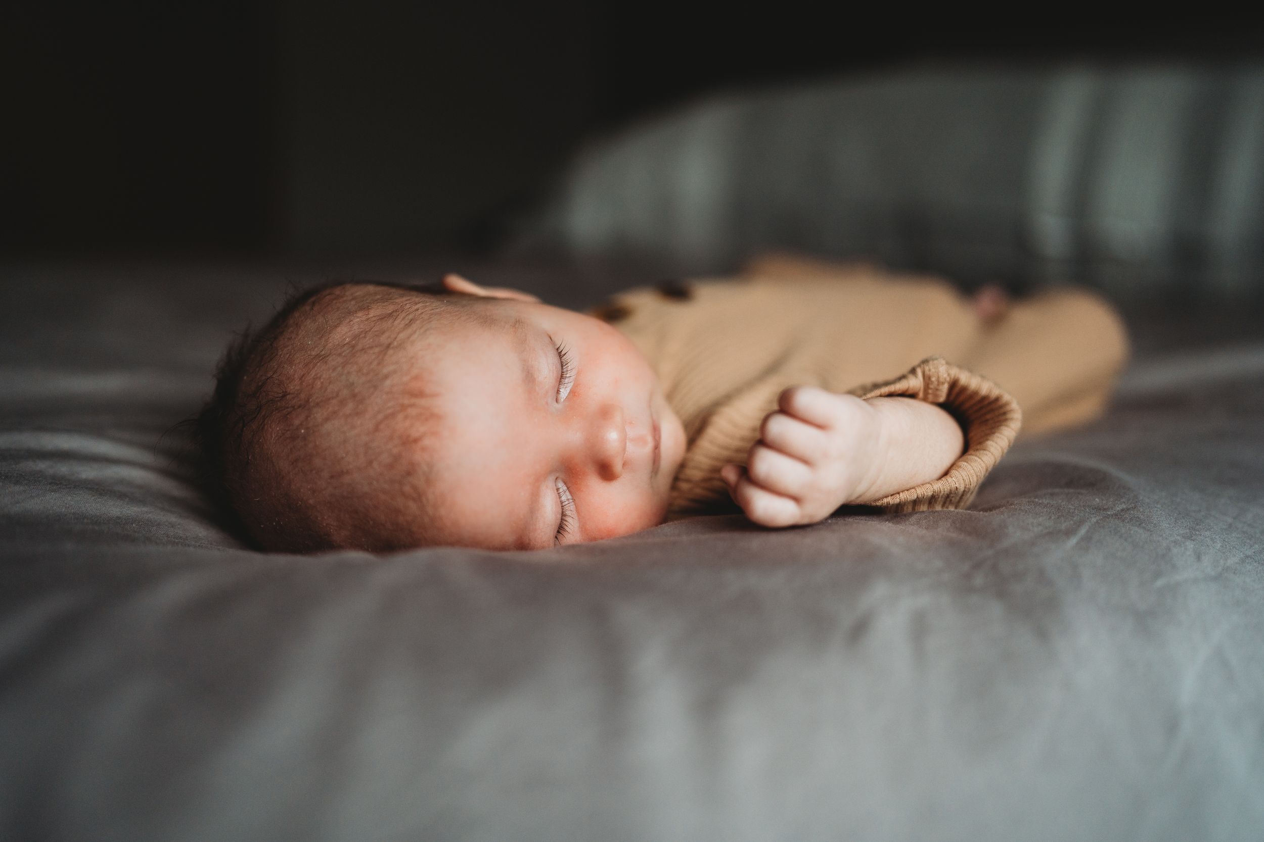 A sleeping newborn baby lies peacefully on grey bedding.