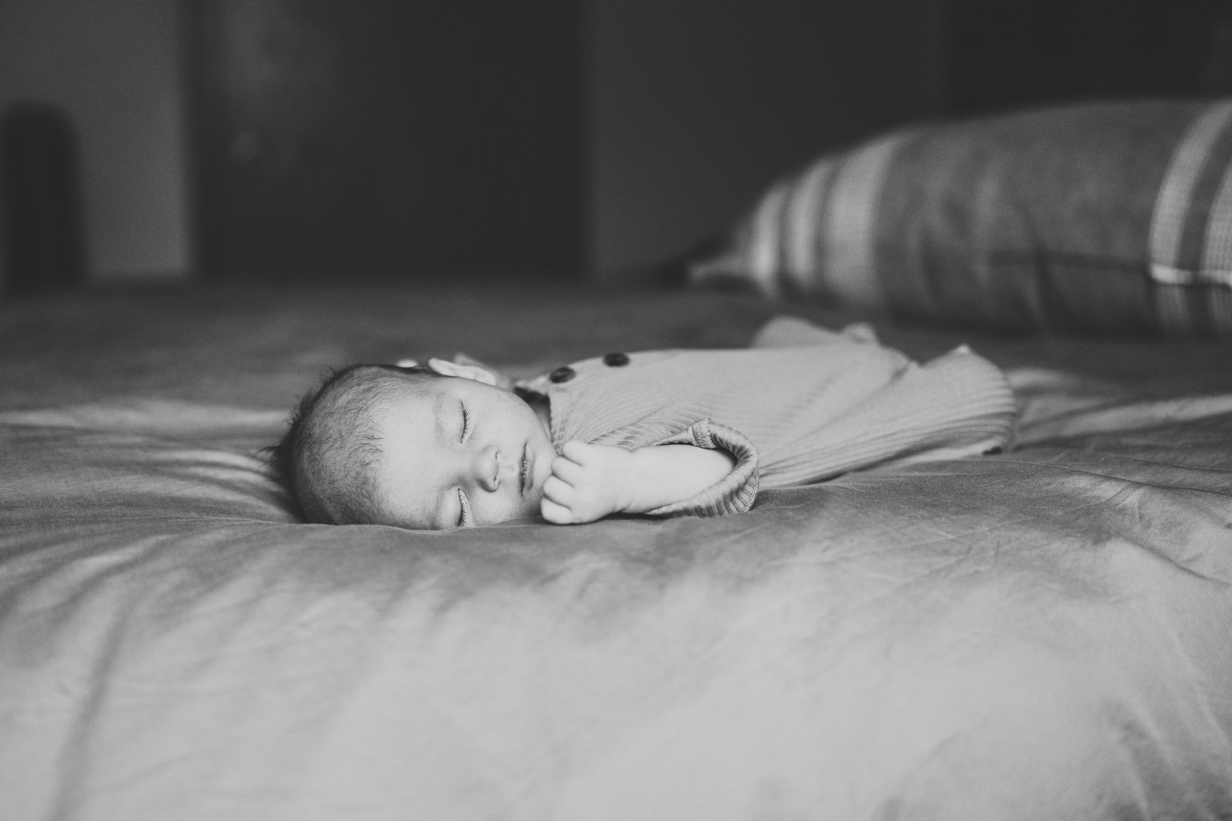 Black and white photo of a sleeping infant on light colored bedding.