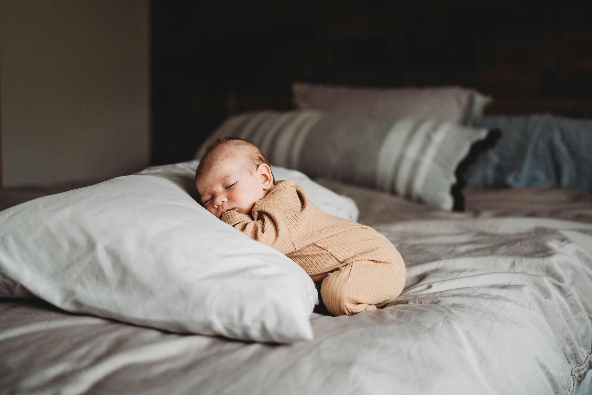 Peaceful baby in tan outfit naps on white pillow and bedding.