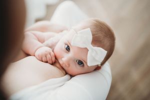 An intimate portrait of a baby with a white bow headband resting peacefully.