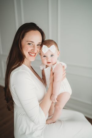Mother and baby share tender moments in white outfits against light backdrop.