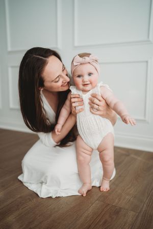 Mother and infant playing together on wooden floor in white outfits.