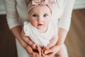 Baby wearing pink bow headband in white outfit.