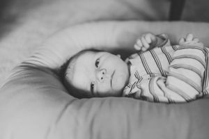 A baby in striped clothing lies on soft bedding in black and white.