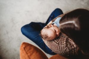 An infant rests peacefully on someone's lap wearing a patterned outfit.