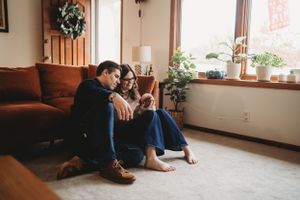 Two people share a moment together on a couch near a window with plants.