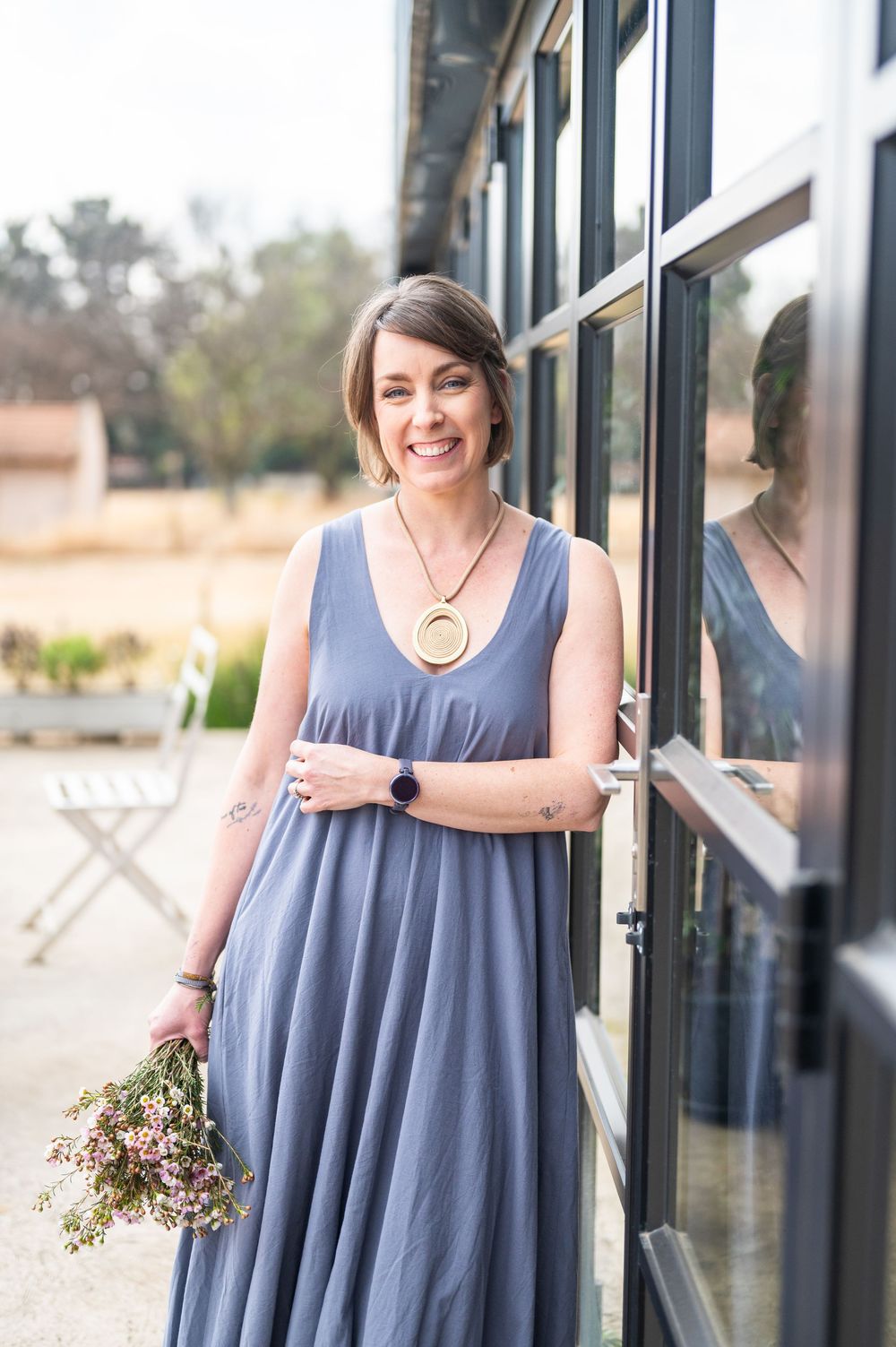 A person in a flowy blue-gray sleeveless dress poses by glass windows in a series of casual portraits.