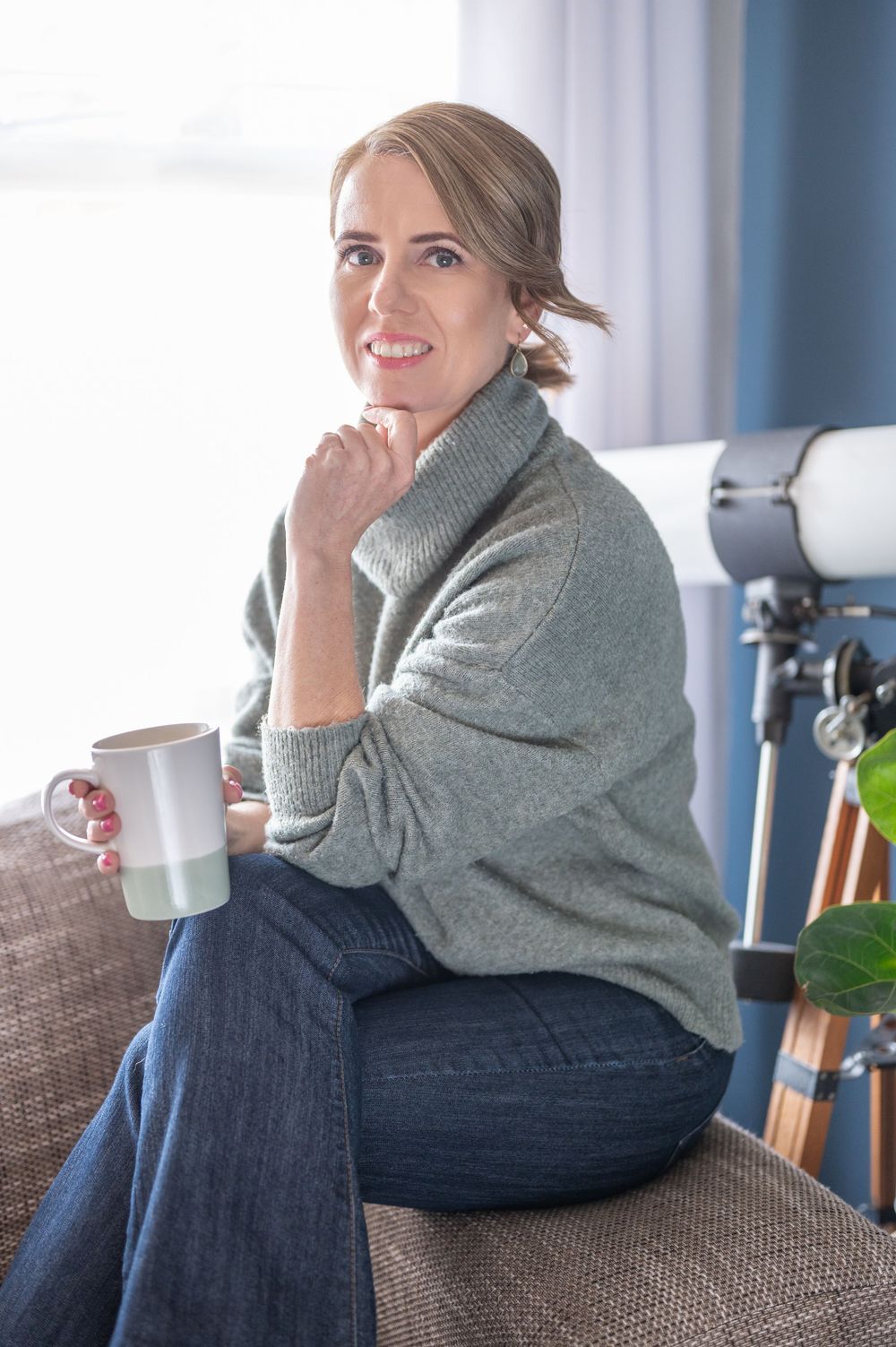 Person wearing a gray sweater and jeans relaxes on a brown couch in a modern interior setting.