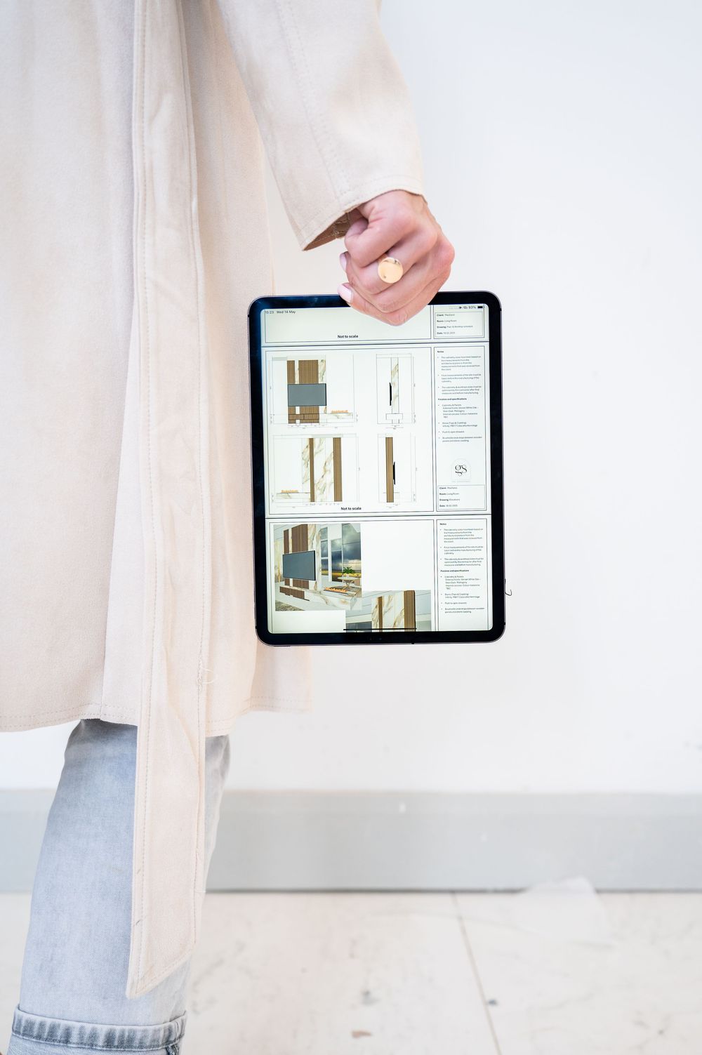 A hand holds a tablet device displaying interior design layouts and floor plans against a light background.