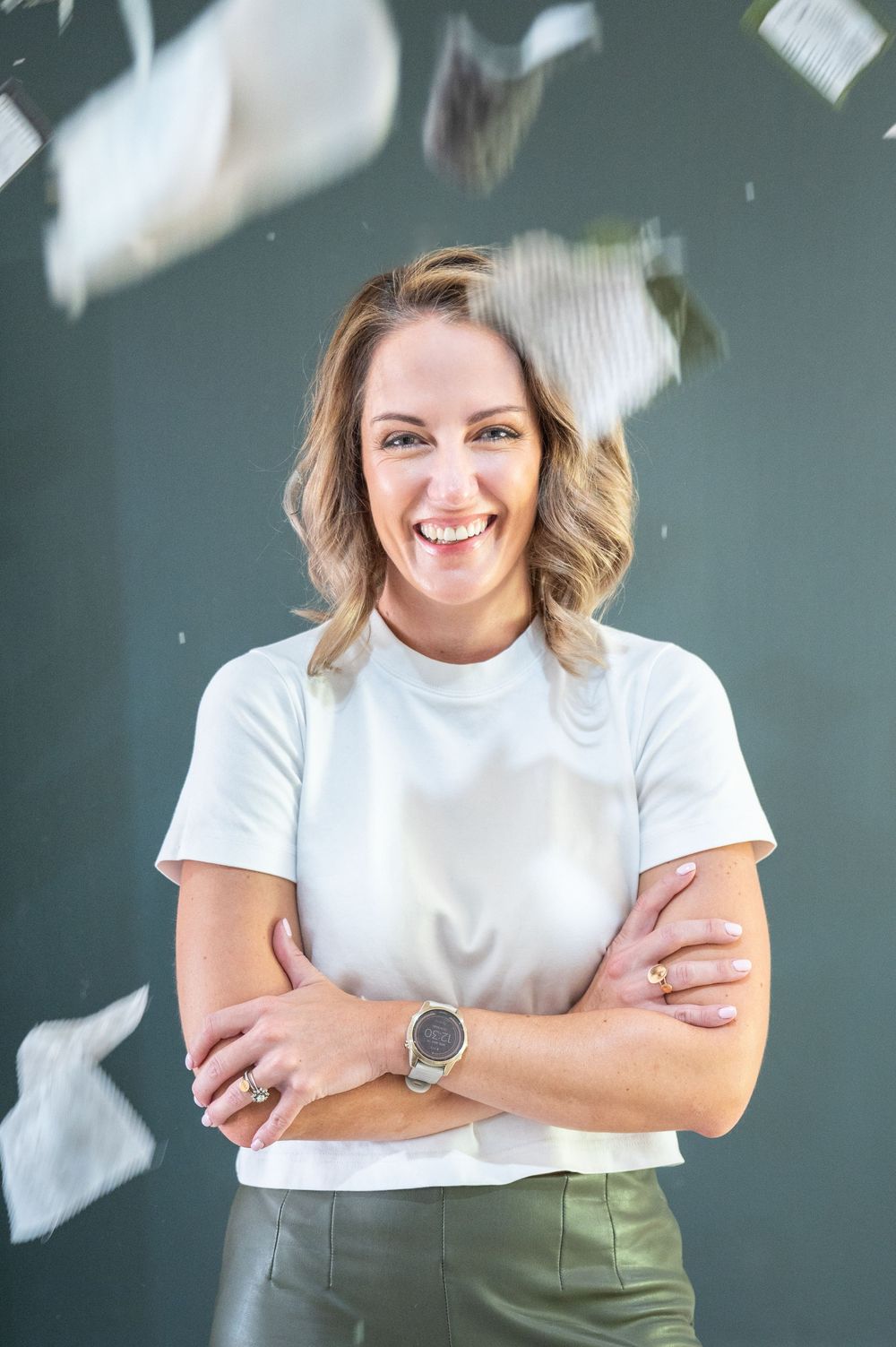 Woman in white shirt smiles confidently with arms crossed while fabric samples float in the air against dark background.