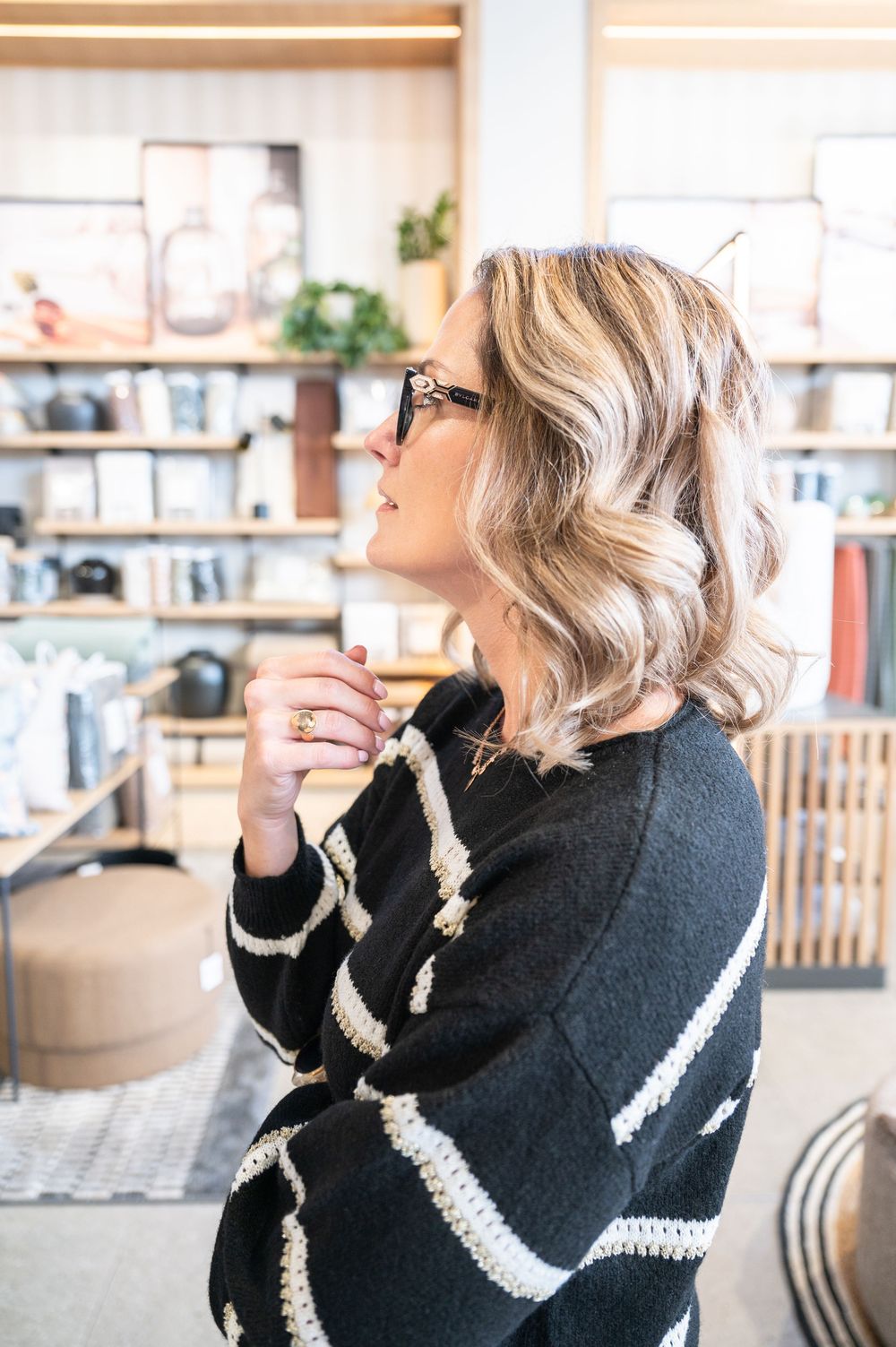 Side profile of woman in black and white striped sweater looking up thoughtfully in modern office setting.