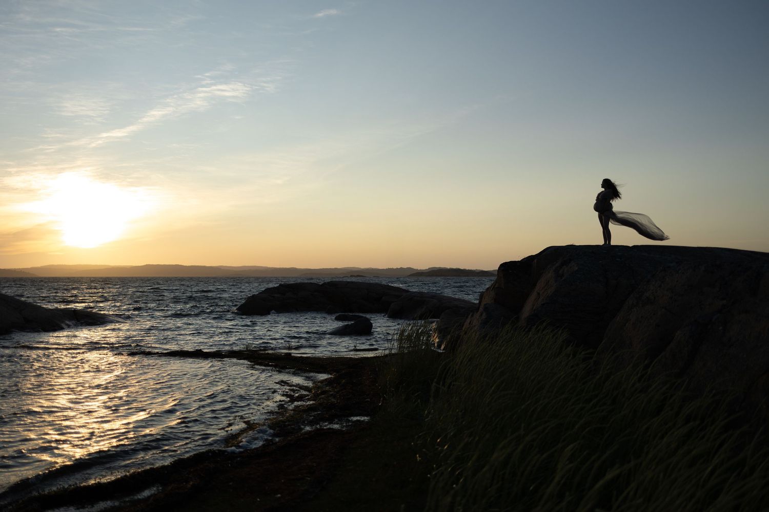 Gravid kvinna i vit spetskimono och med alvisk krona sitter på en klippa och blickar ut över havet