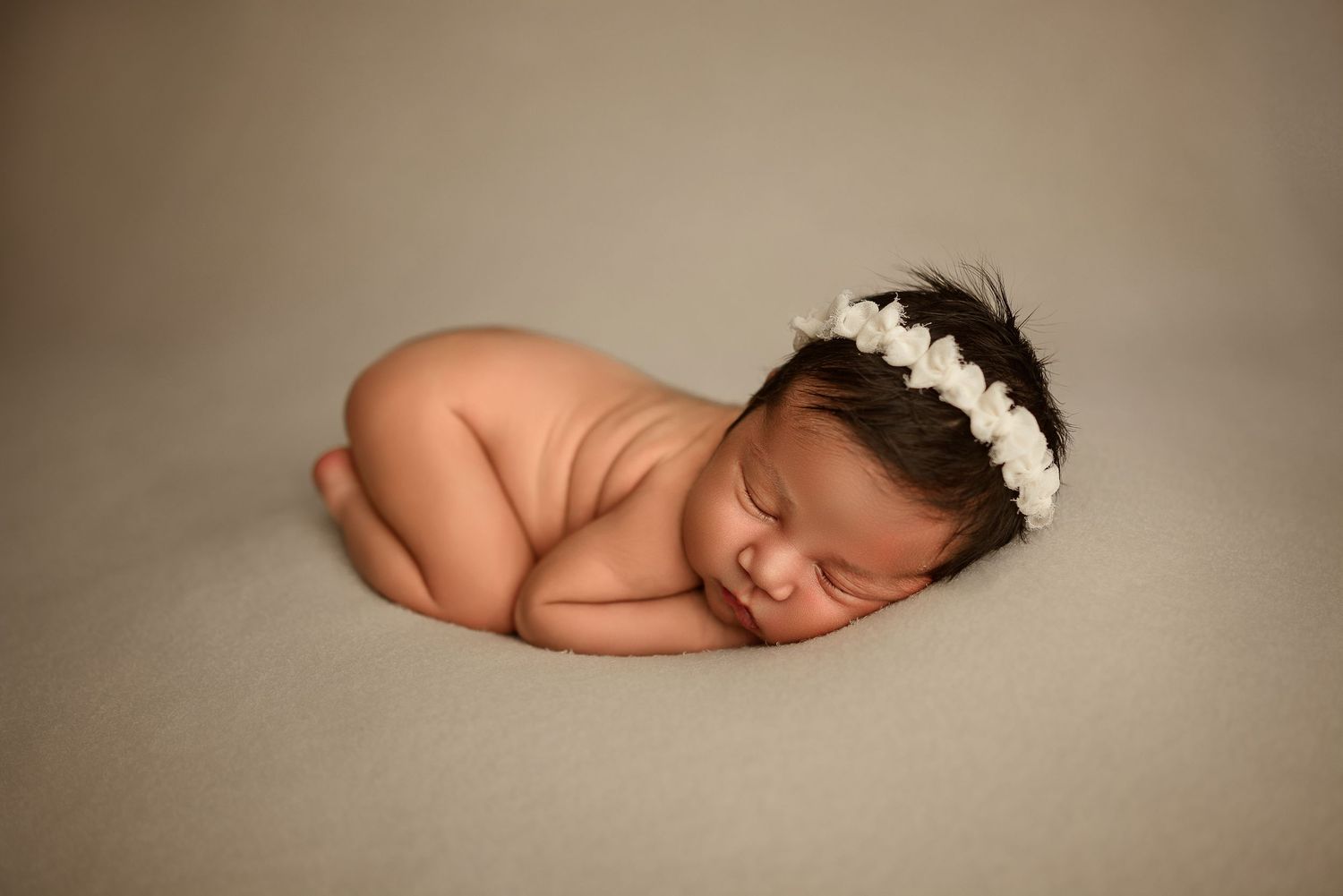 Newborn baby girl sleeps peacefully on cream backdrop during studio newborn session in Clarksville, Tennessee by Disney Magic Photography.