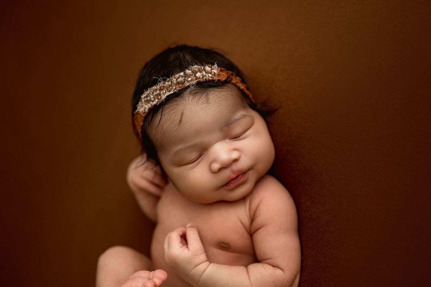 Newborn baby girl sleeps peacefully on rust colored backdrop in Clarksville, Tennessee newborn photography studio