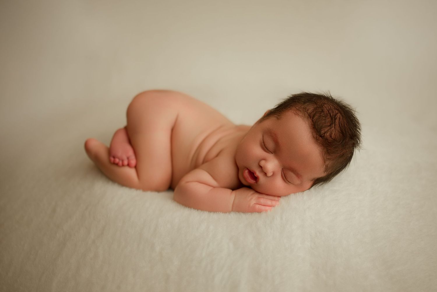 Newborn baby boy sleeps peacefully on cream backdrop during studio newborn session in Clarksville, Tennessee by Disney Magic Photography.