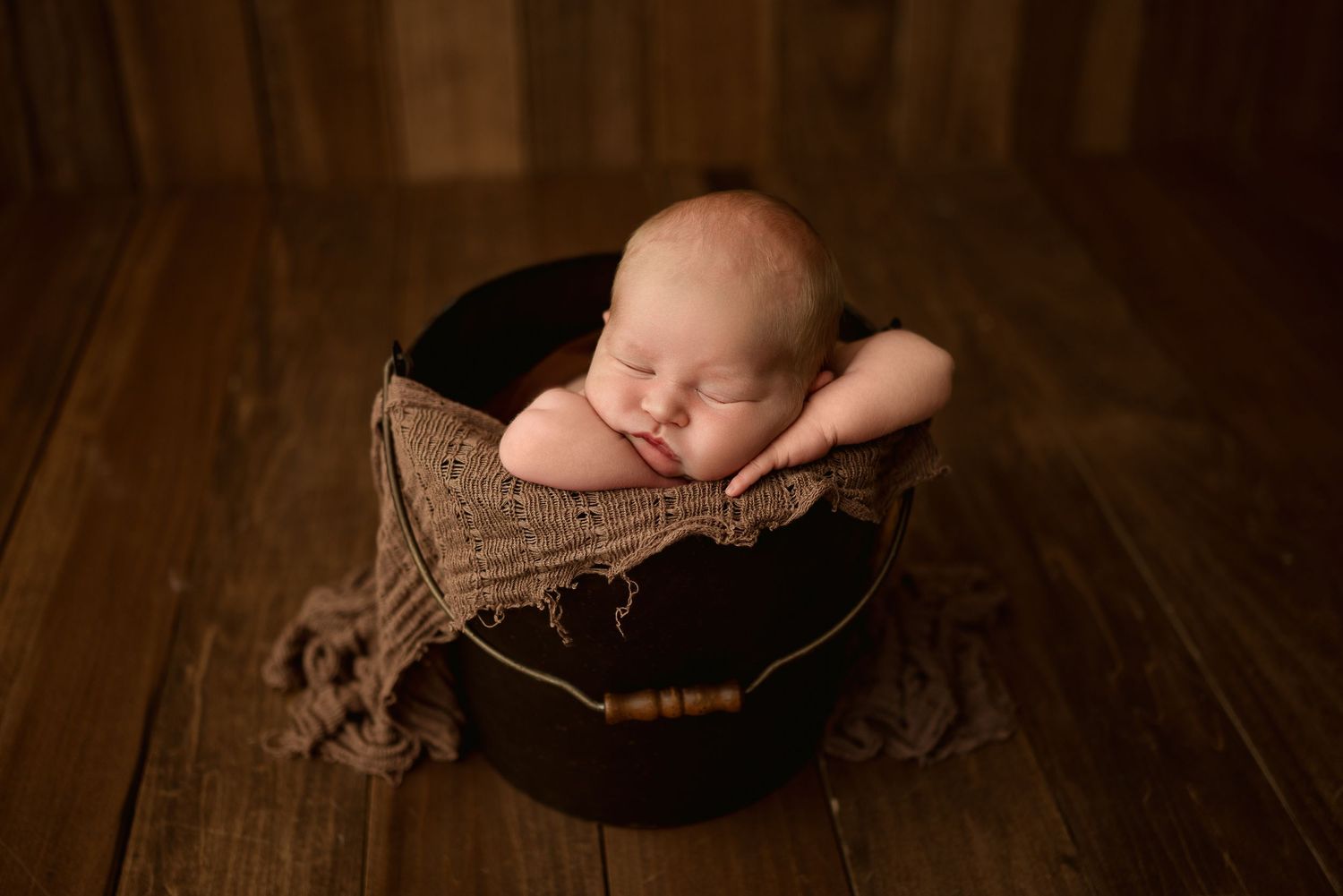 Newborn baby boy sleeps peacefully in rustic bucket during studio newborn session in Clarksville, Tennessee by Disney Magic Photography.