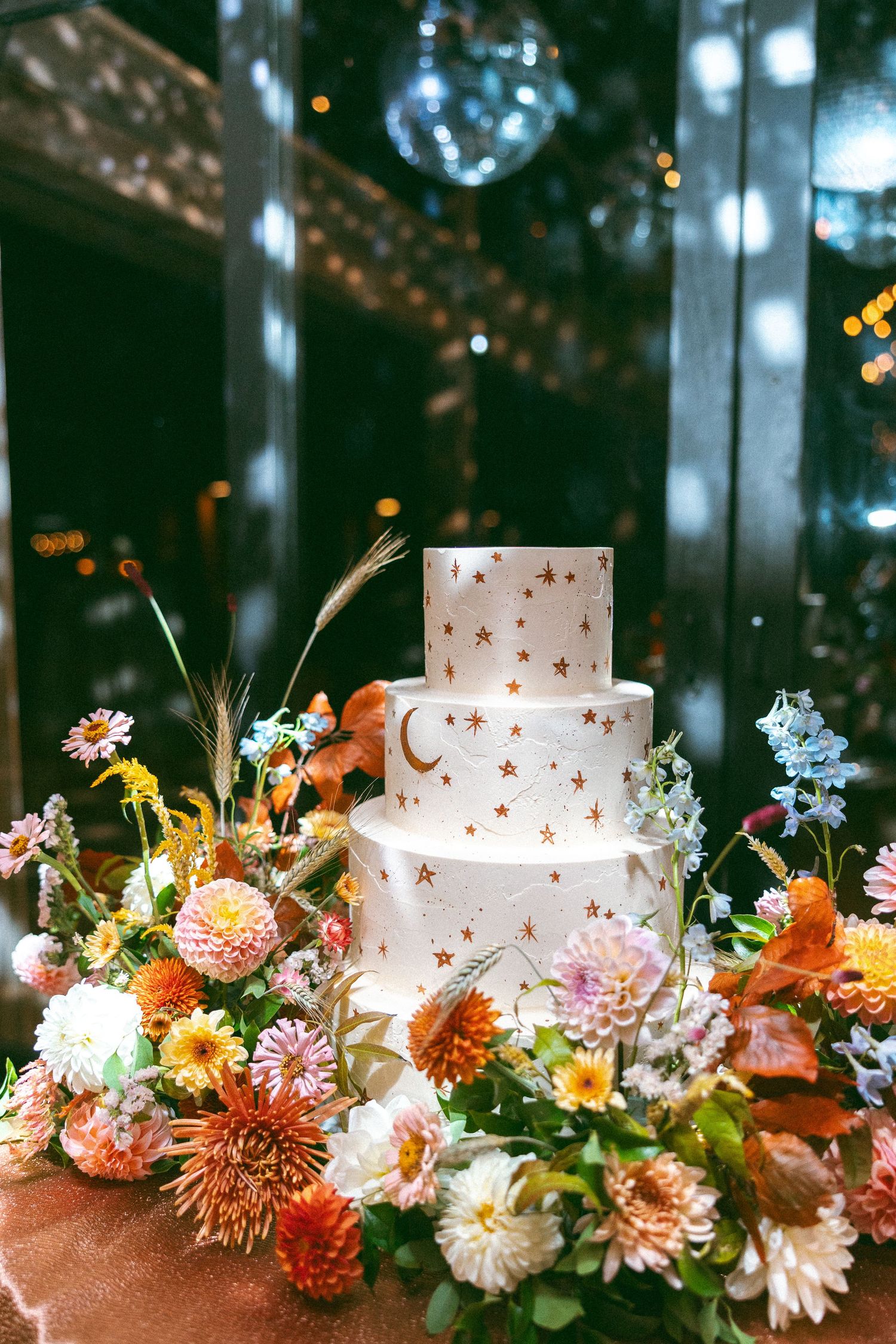 Elegant white wedding cake decorated with fresh autumn flowers and soft lighting.