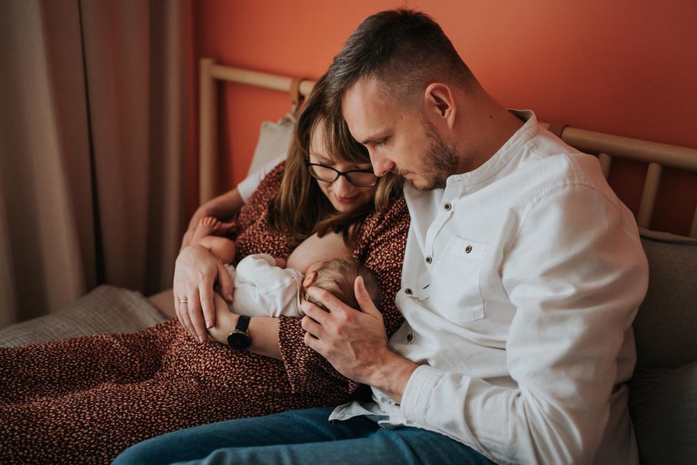 mama i tata siedzą na łóżku z noworodkiem - sesja rodzinna Kraków