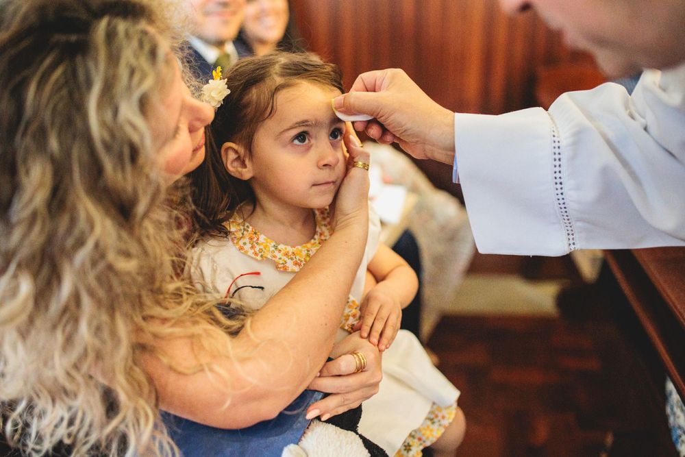 A person places ashes on a young child's forehead during a religious ceremony as another person holds them.
