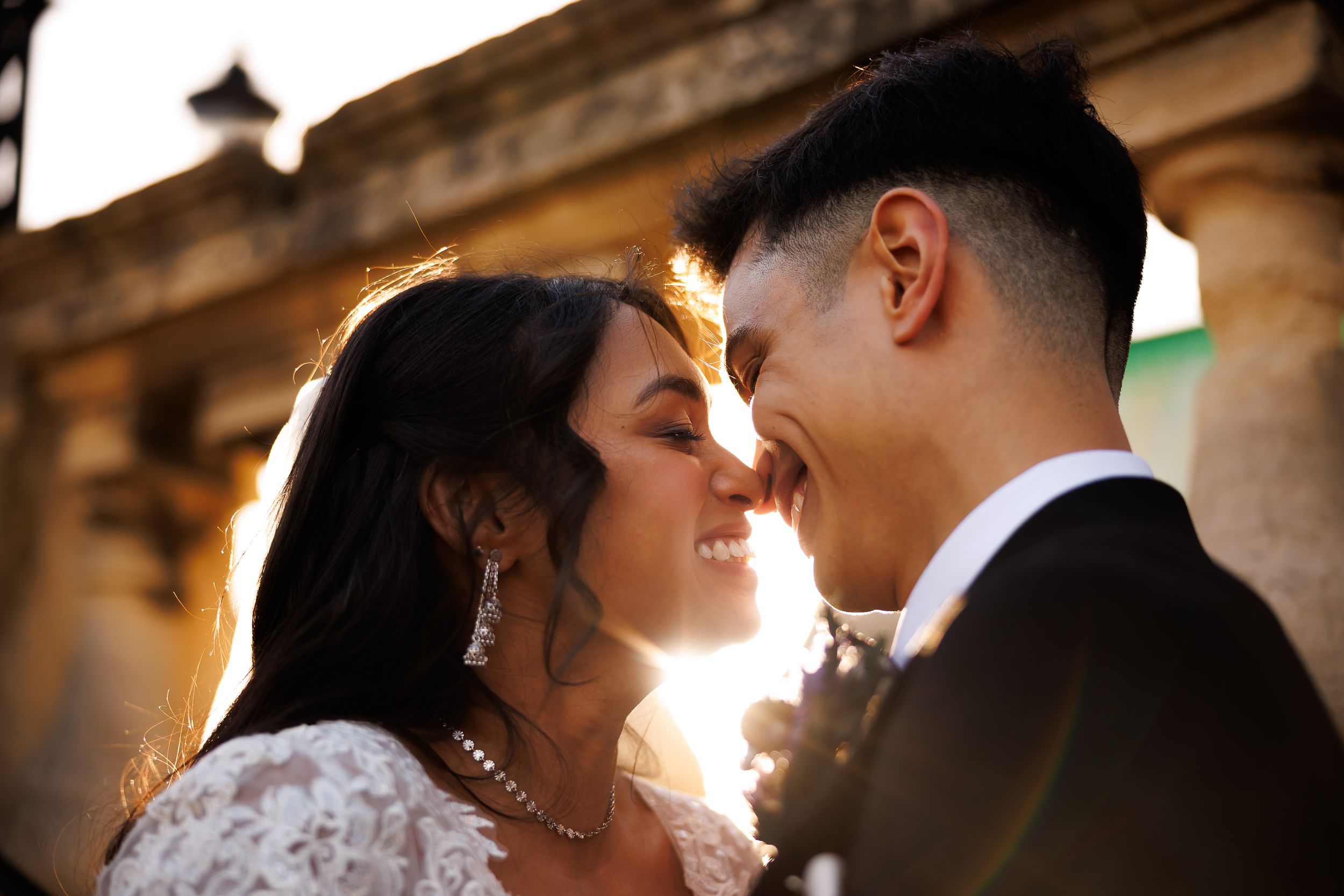 Romantic couple embraces in golden sunlight during wedding photoshoot creating silhouetted profiles against warm glow.