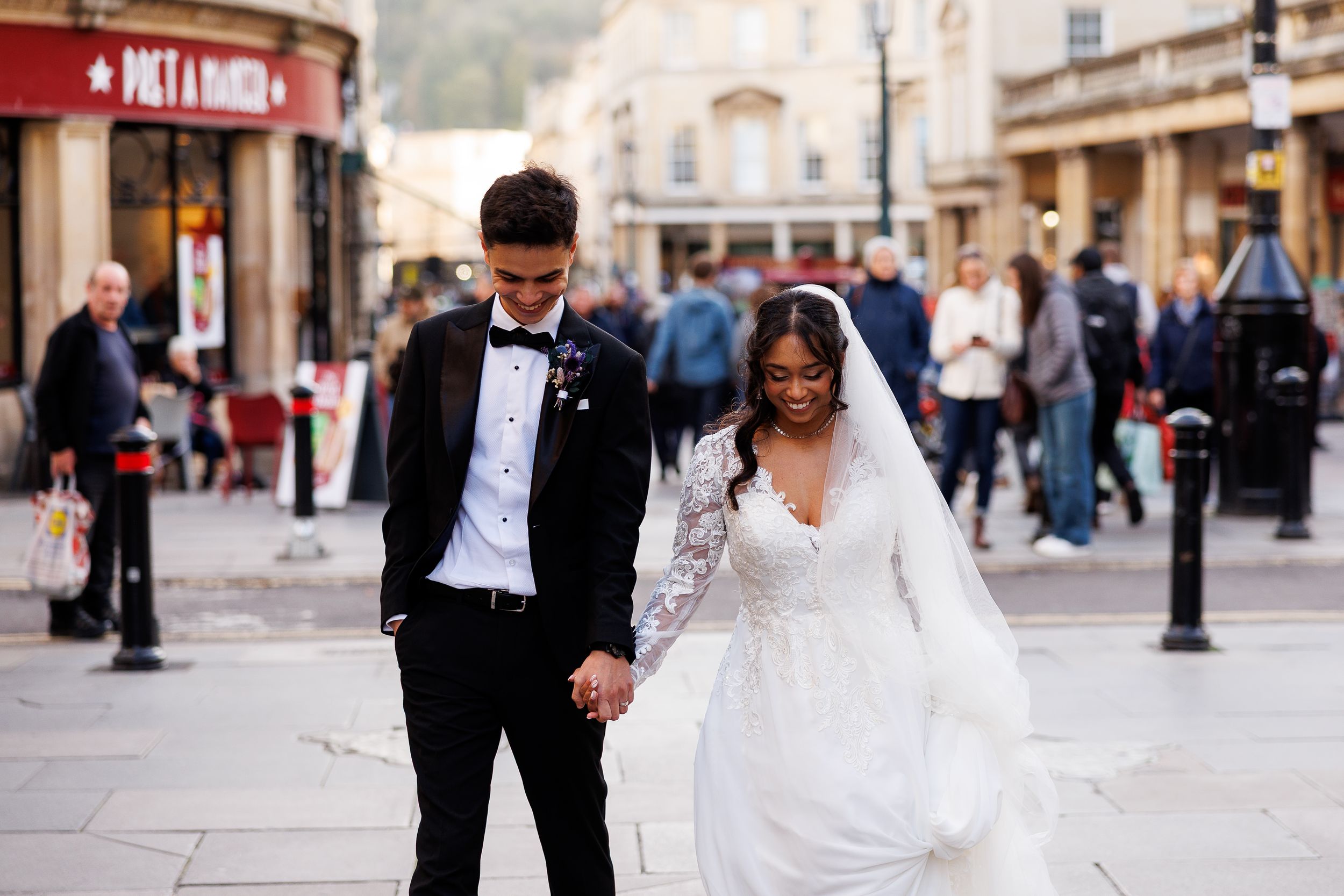A couple in formal wedding attire walks together on a cobblestone street during their special day.