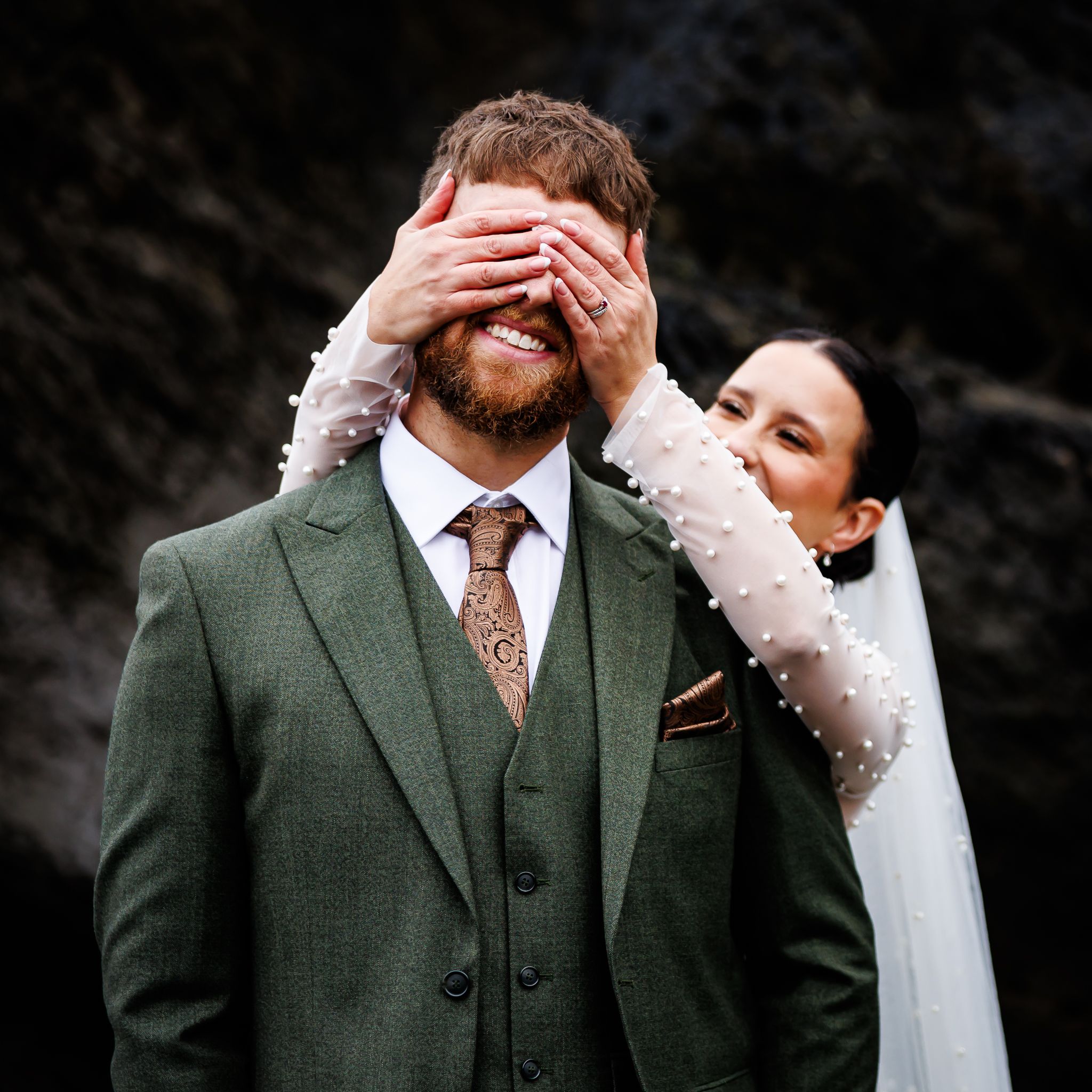 Playful moment between newlyweds as bride covers groom's eyes from behind.