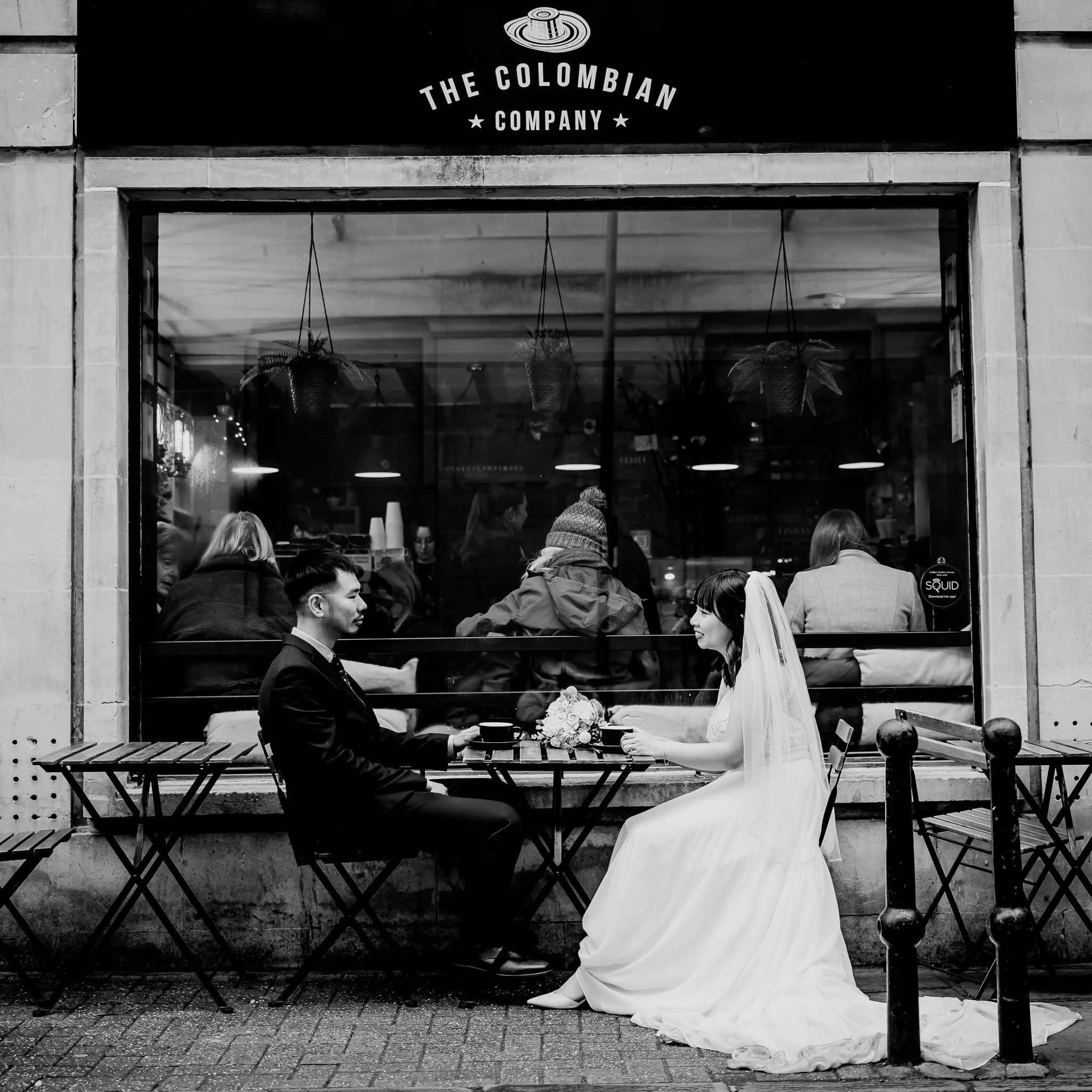 Black and white photo of couple dining outside a cafe with The Colombian Company storefront.