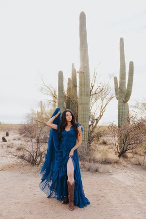 Elegant blue dress contrasts with tall saguaro cacti in a desert setting.