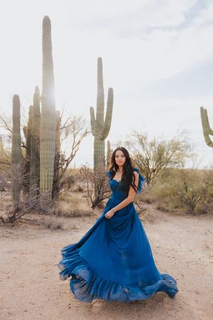 Navy dress twirls dramatically against backdrop of desert cacti and sand.