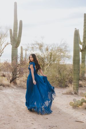 Flowing blue dress movement captured in desert setting with tall saguaro cacti.