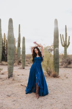 Dramatic blue gown photoshoot among towering saguaro cacti in desert landscape.