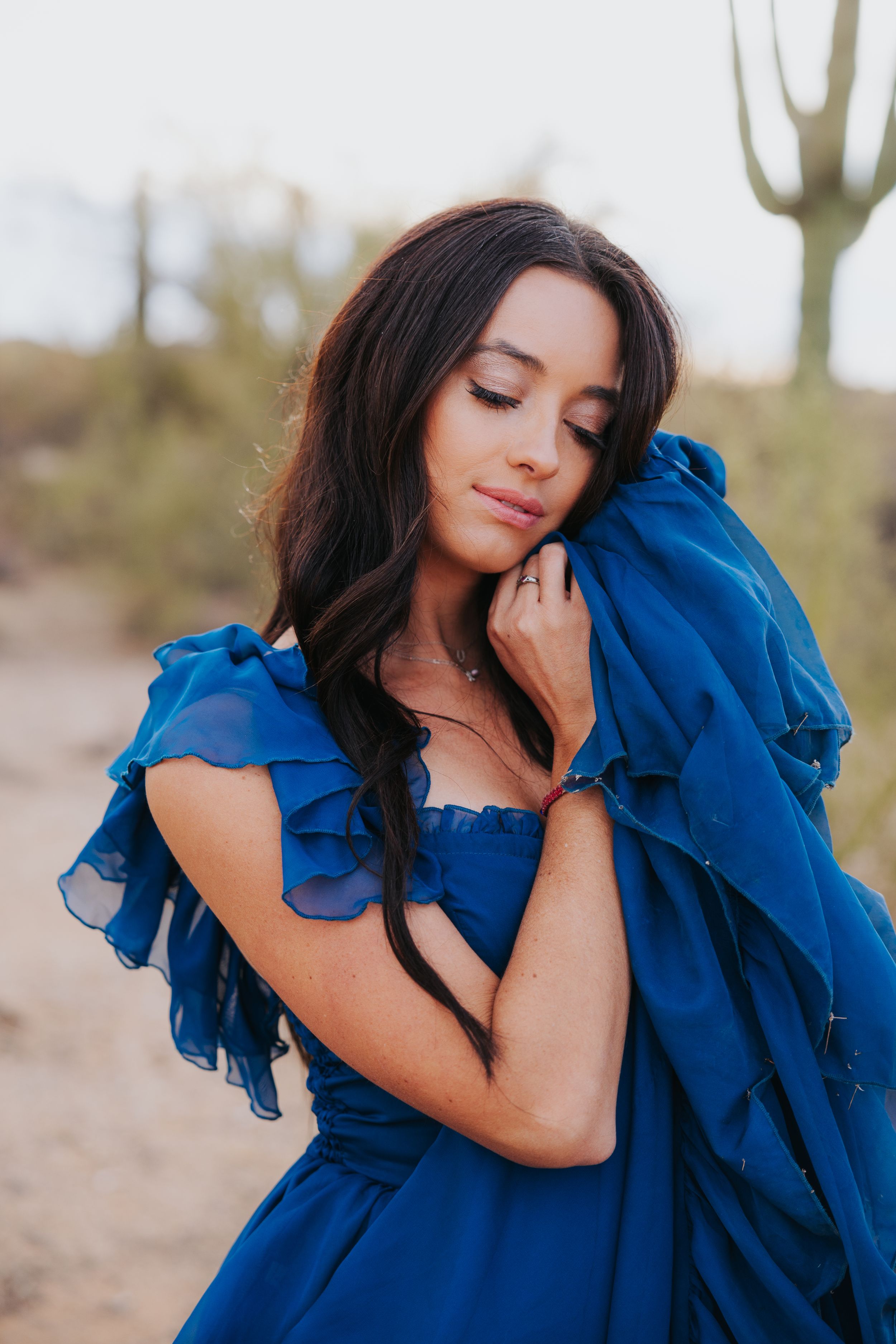 Fashion portrait series in a flowing royal blue dress against a desert backdrop with saguaro cacti.