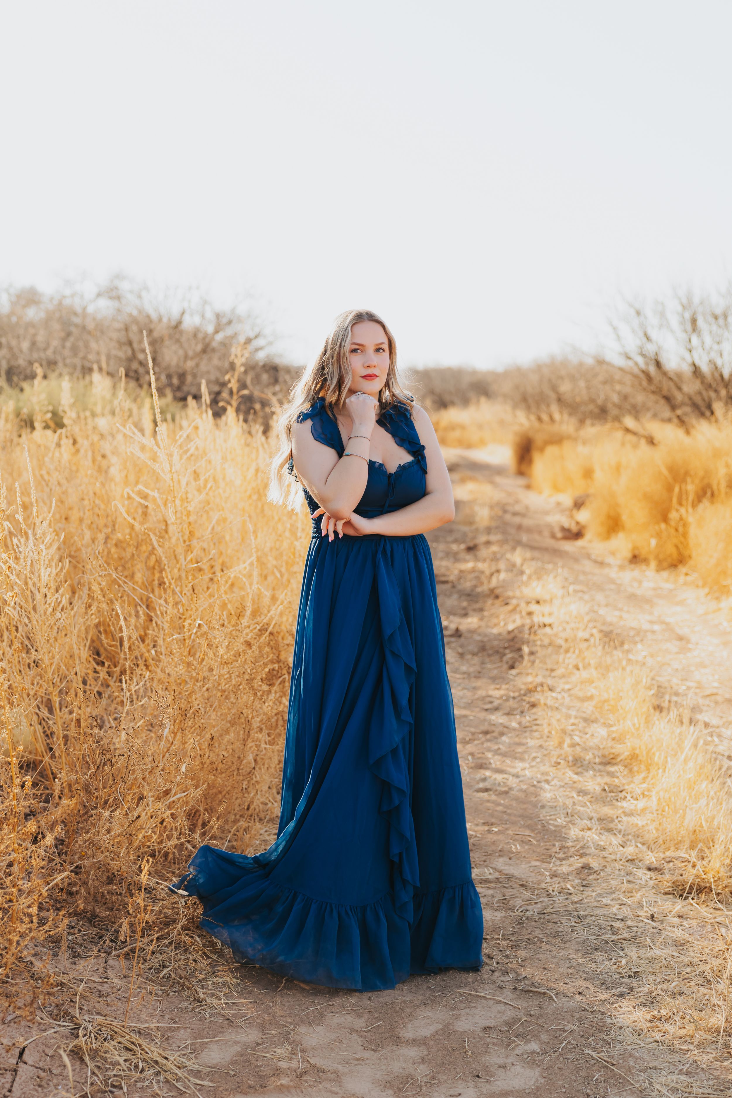 Navy blue dress flows elegantly along desert path with golden brush.