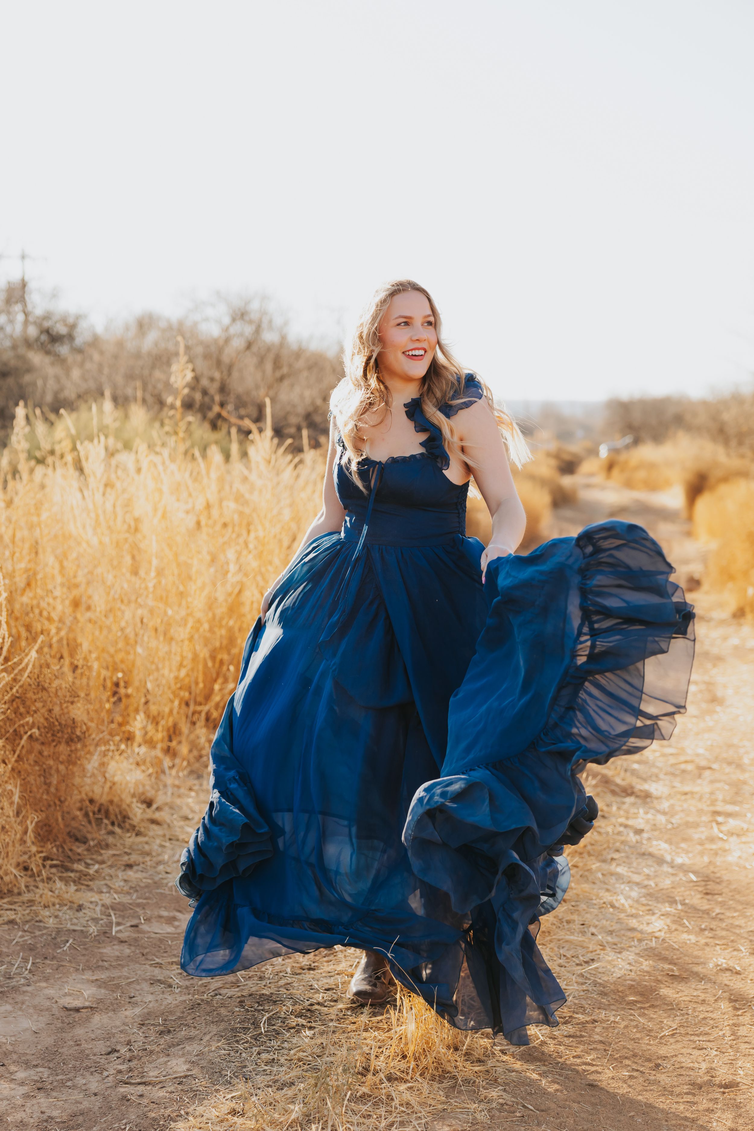 Flowing navy dress twirls dramatically on desert trail during golden hour.