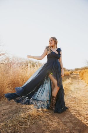 A flowing navy blue dress billows dramatically against a desert landscape with golden grass.