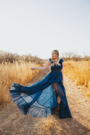 Navy blue gown swirls gracefully on a dirt path surrounded by dry golden grass.