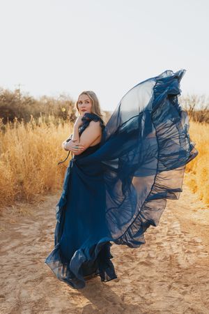 Dramatic navy blue gown flows in the wind along a desert trail.